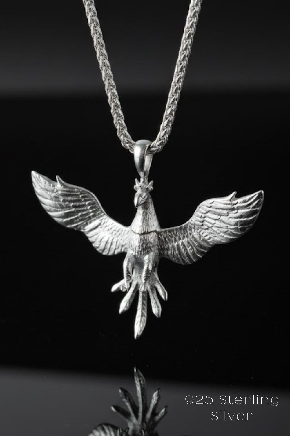 A silver pendant necklace with a detailed design of a winged bird, possibly a phoenix, suspended from a chain.