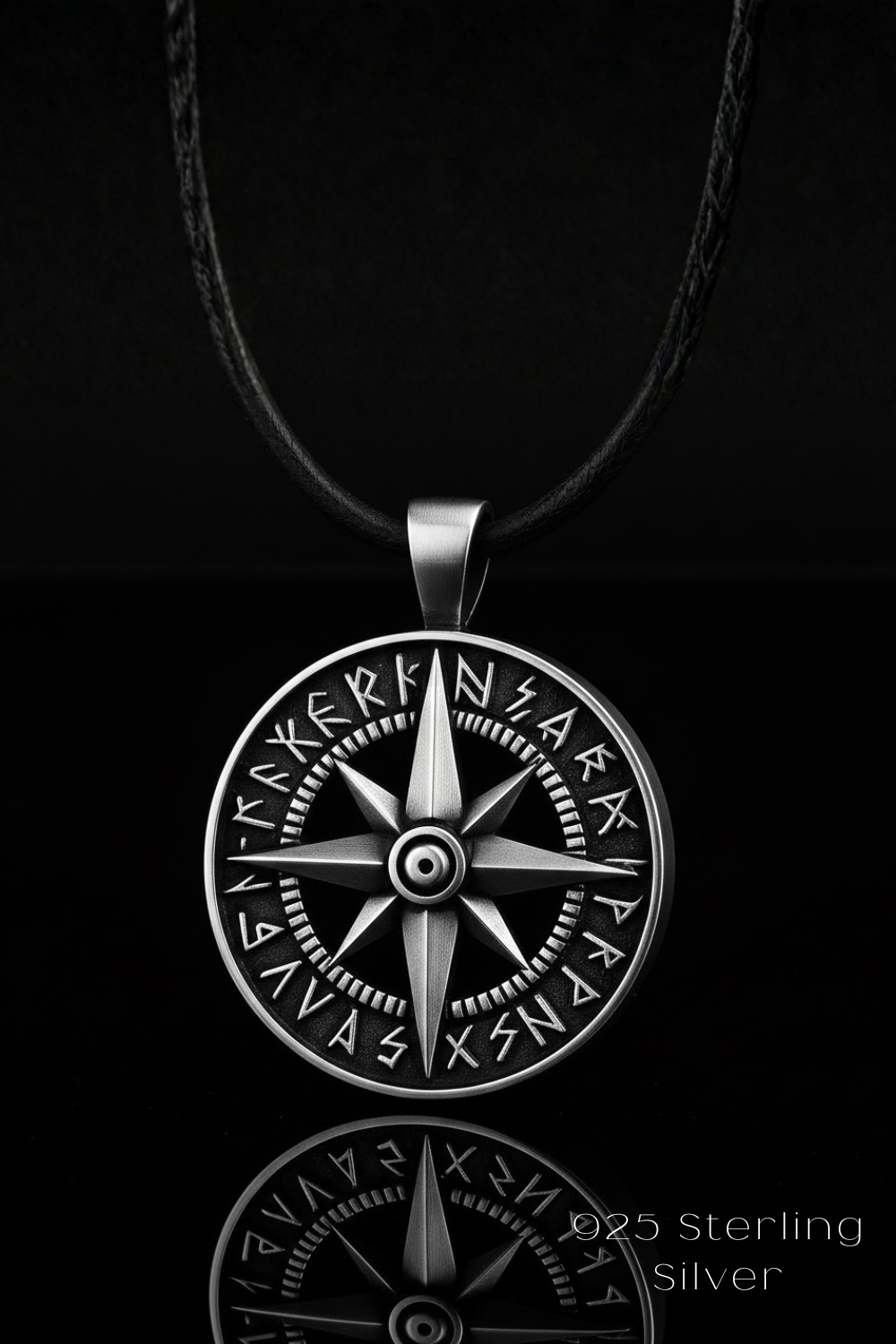 A silver compass pendant with intricate engravings, suspended from a black cord against a dark background.