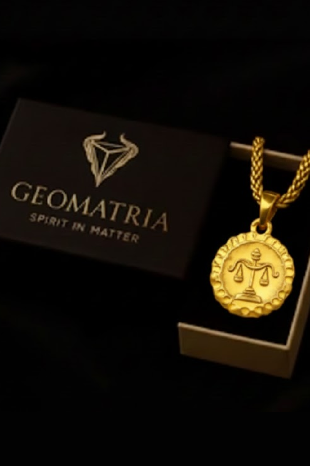 a gold necklace with a pendant, placed inside a black box with the word "Geomatria" printed on it.