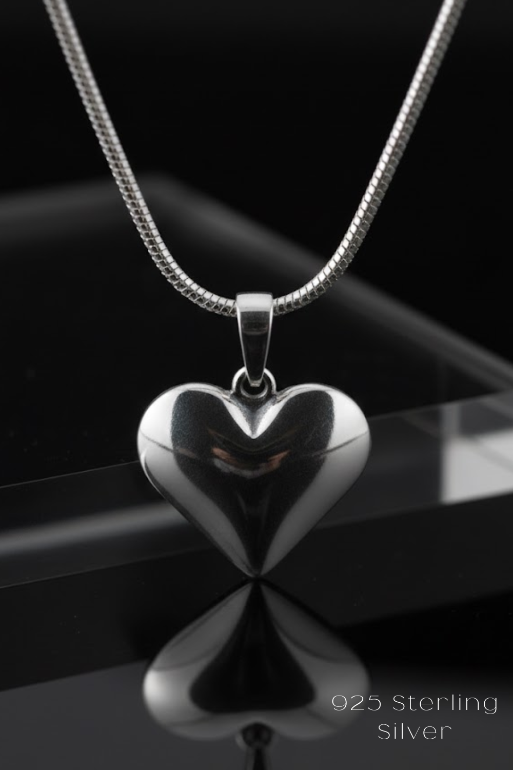 A silver heart-shaped pendant necklace with a silver chain is displayed against a black background.