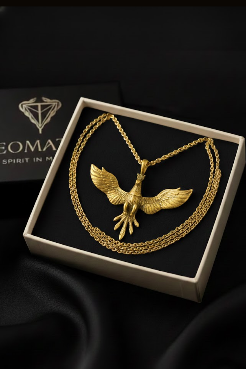 A gold-colored pendant necklace with a bird-like design is displayed in a white box against a black background.