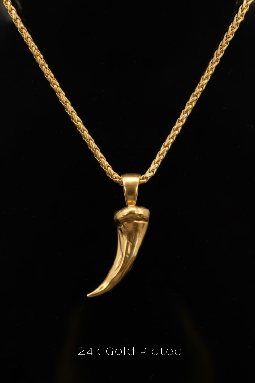 A gold-plated pendant in the shape of a horn or tusk is displayed against a black background.