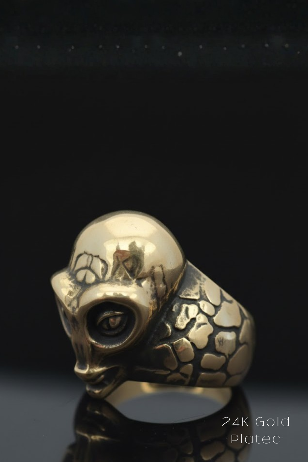 a gold ring with a skull-like design, set against a black background.