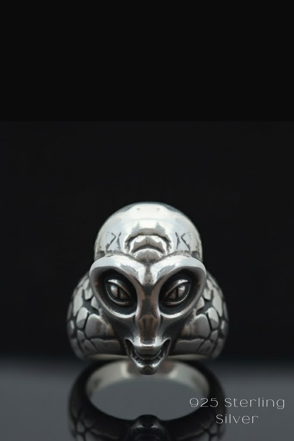 A silver ring with an alien or alien-like face design, set against a black background.