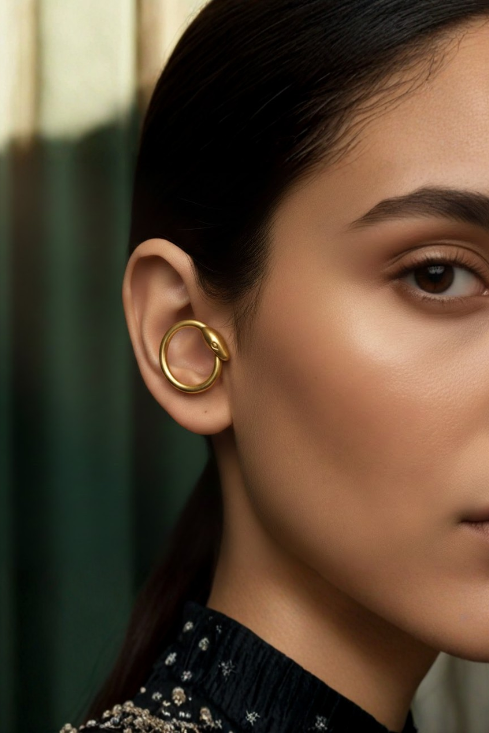 A close-up of a woman's face, focusing on her ear and cheek area. She is wearing a gold earring with a snake design.