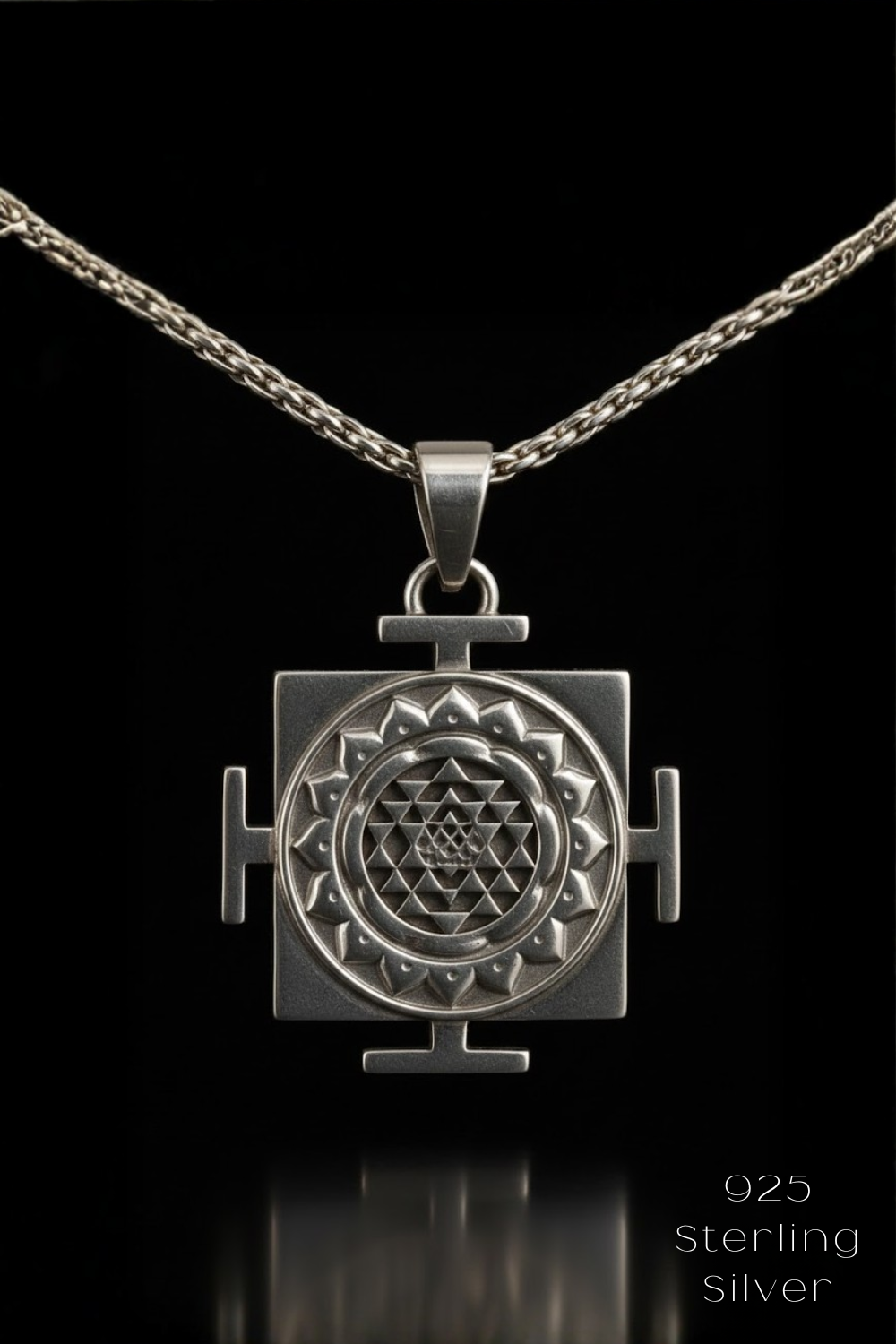 A silver pendant with a geometric design, suspended from a chain against a black background.