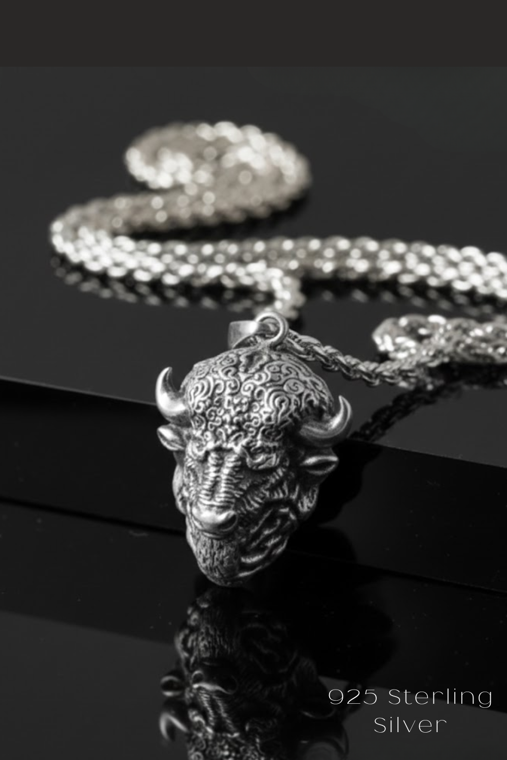 A silver pendant necklace with a detailed buffalo head pendant is displayed against a black background.