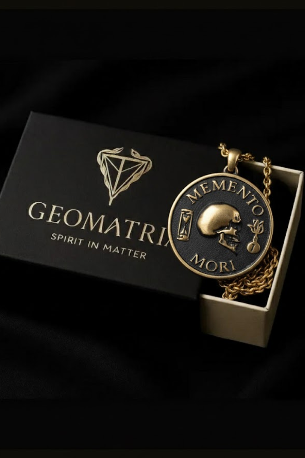 a gold-colored pendant with a skull design, placed inside a black box with the word "Geomatrix" printed on it.