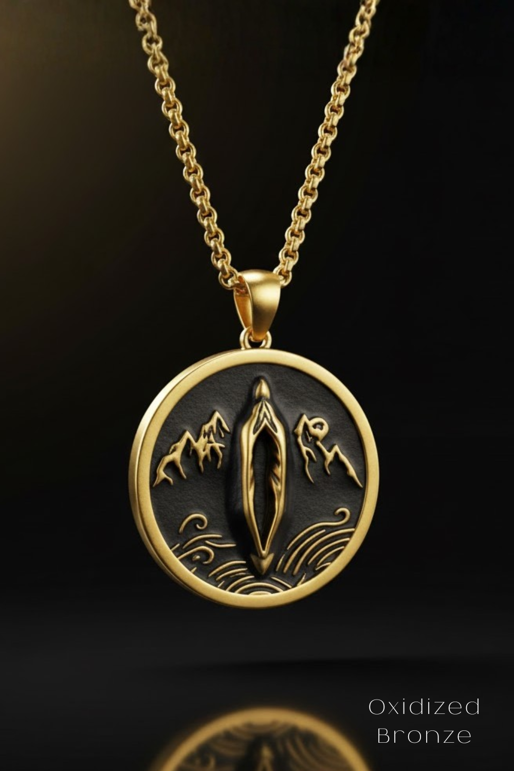 A gold-colored pendant necklace with a circular design featuring a central motif surrounded by mountains and waves.