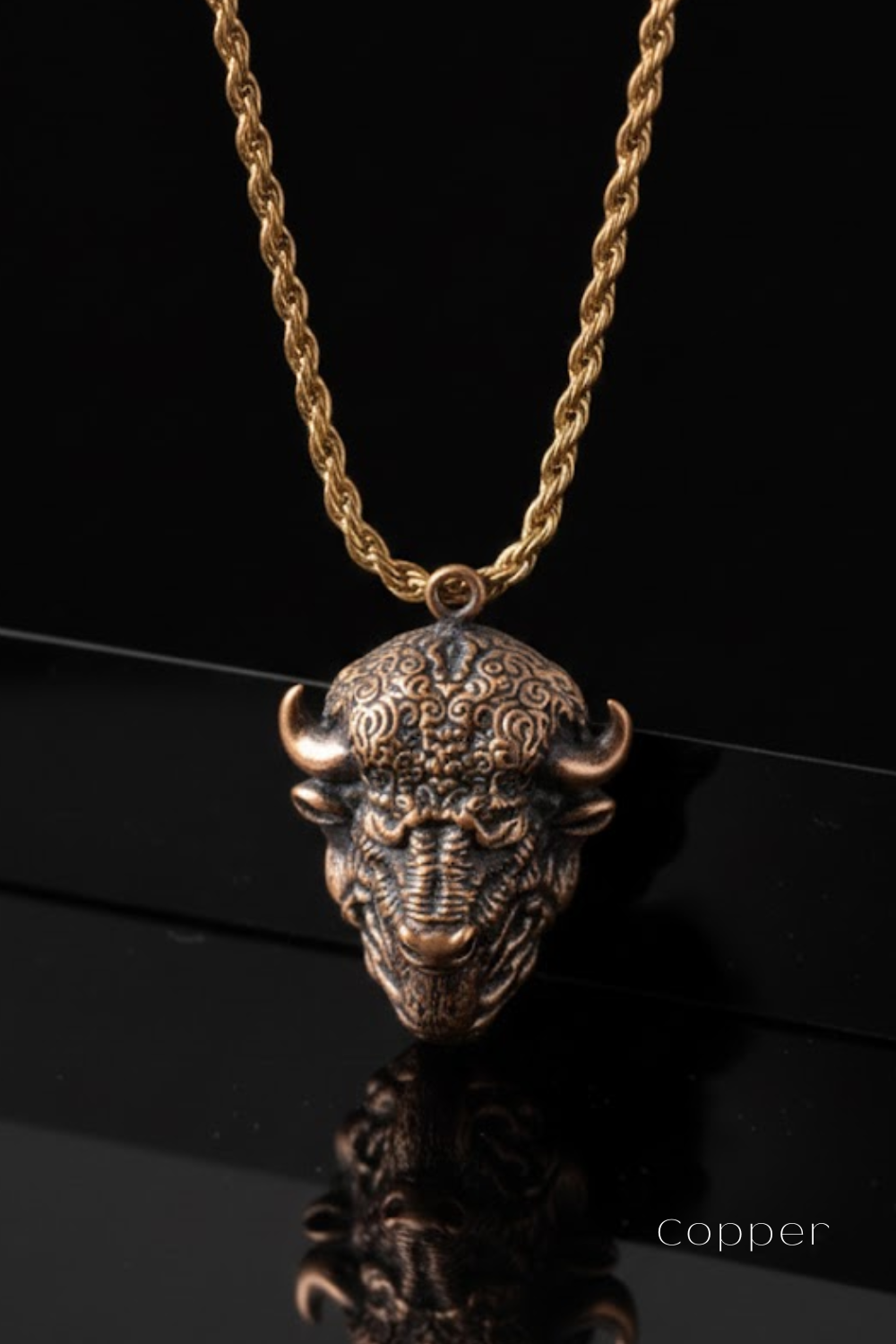 A gold-colored necklace with a pendant in the shape of a buffalo head, which appears to be made of copper.