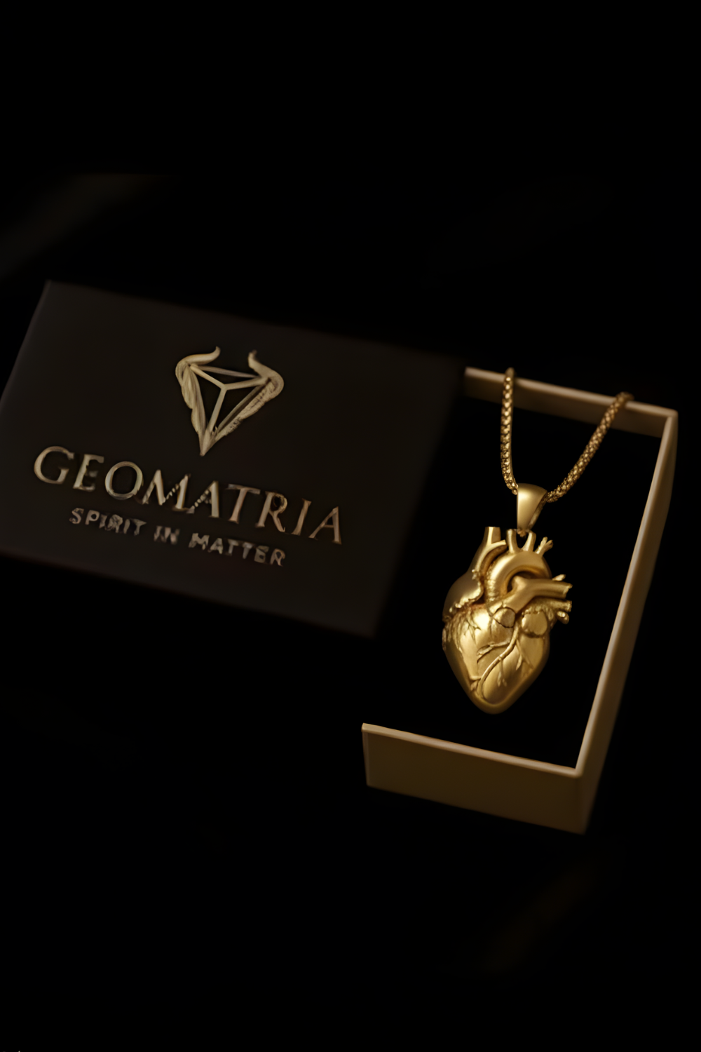 A gold heart-shaped pendant necklace is displayed in a black box with the text "Geomatria" and "Spirit in Matter" printed on it.