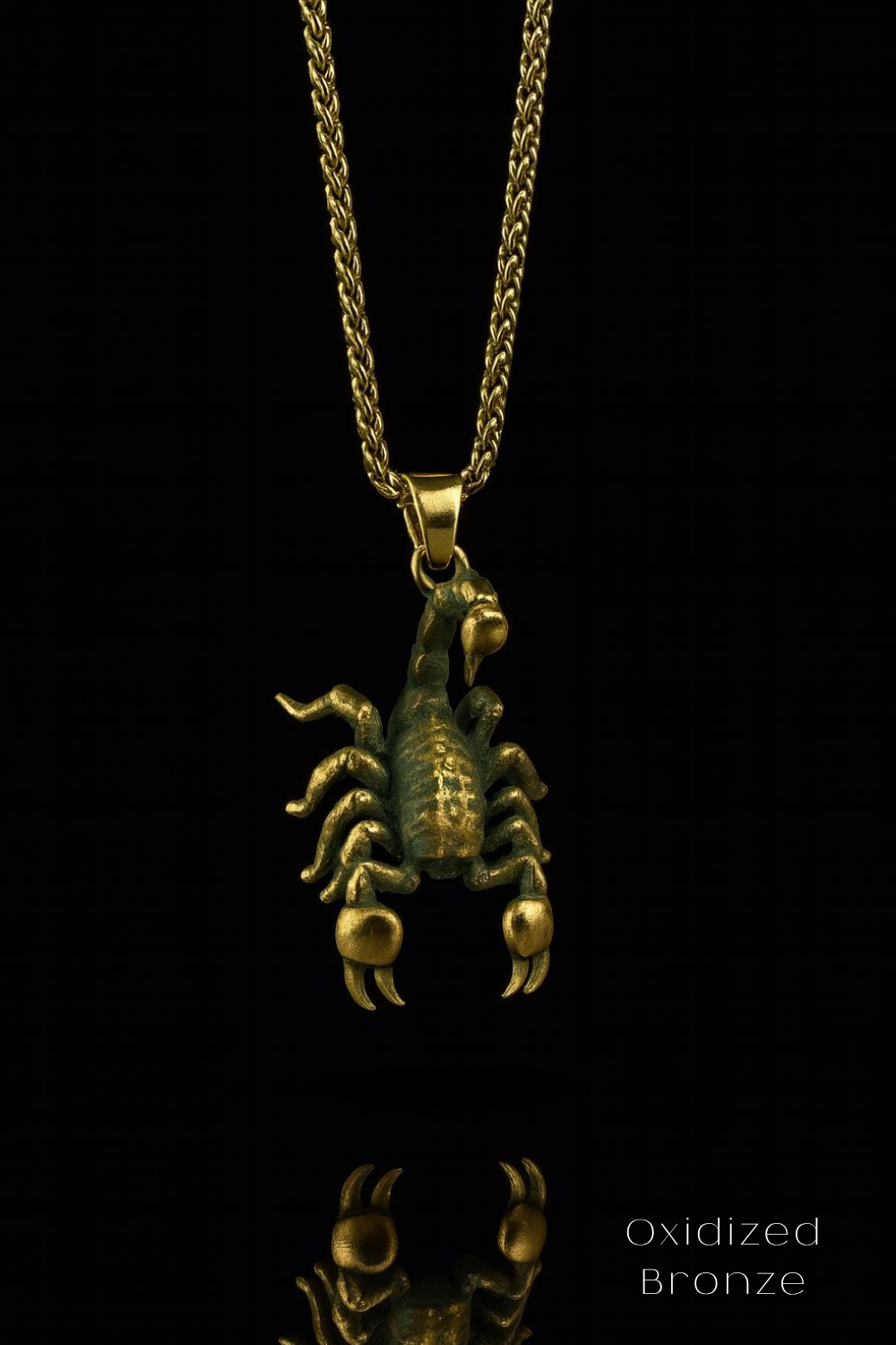 A gold-colored pendant in the shape of a scorpion is displayed against a black background, with a chain necklace visible.