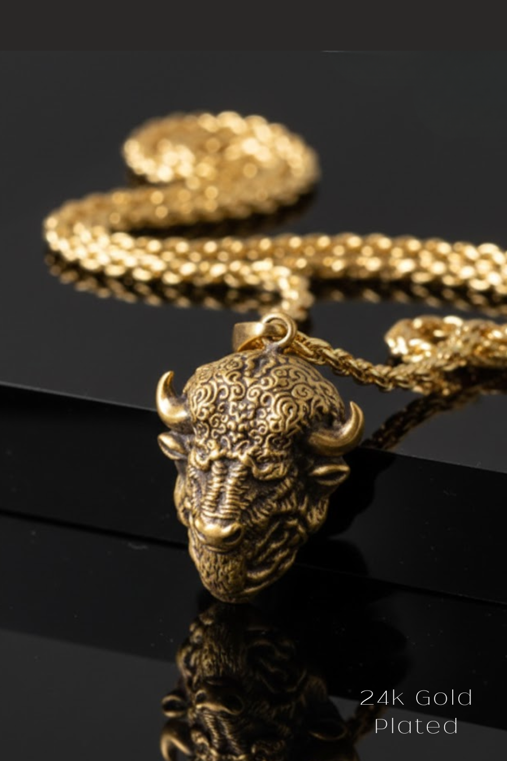 A close-up image of a gold-plated pendant featuring a detailed buffalo head design, with a chain visible in the background.