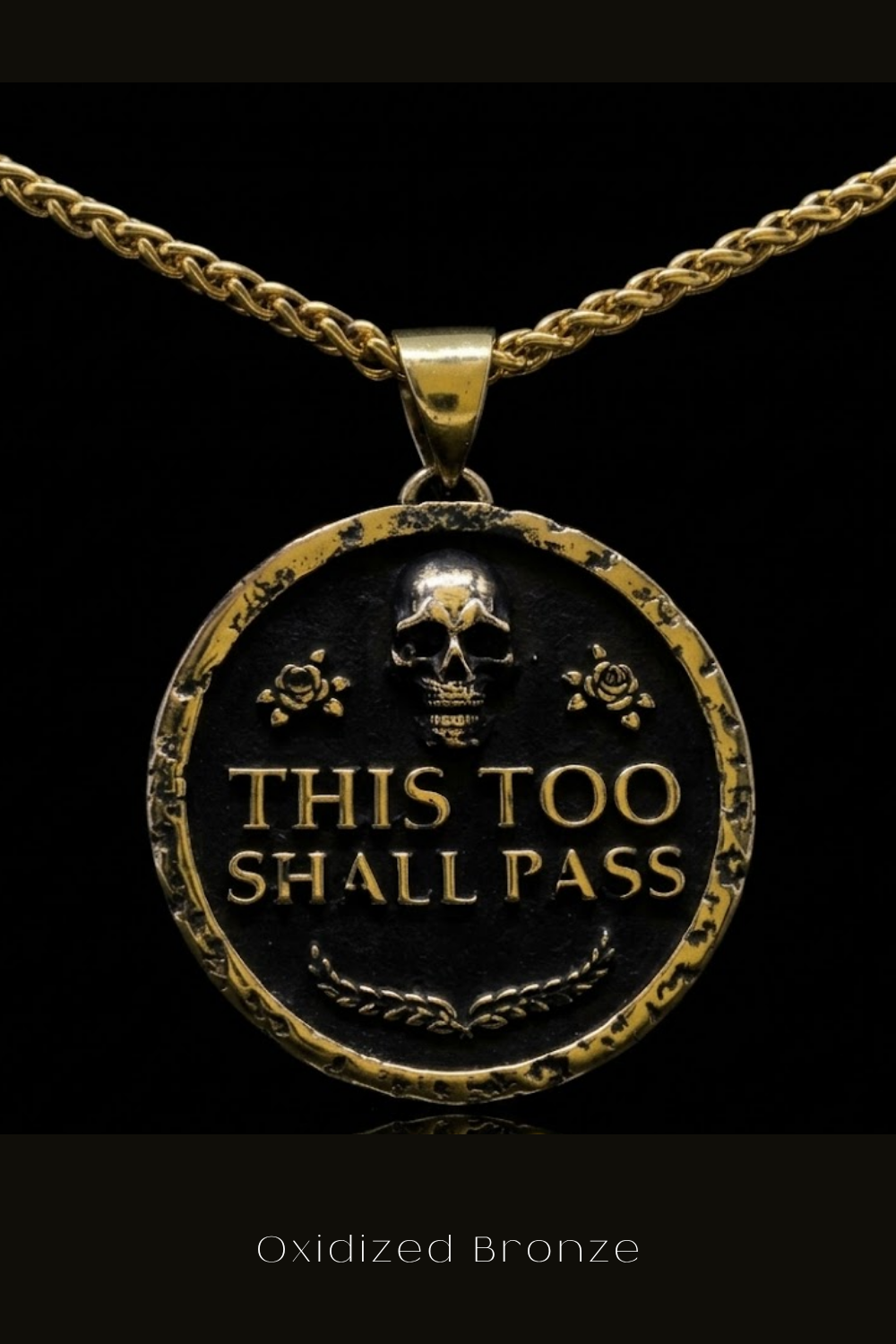 a pendant with the text "This Too Shall Pass" engraved on it, surrounded by a decorative border.