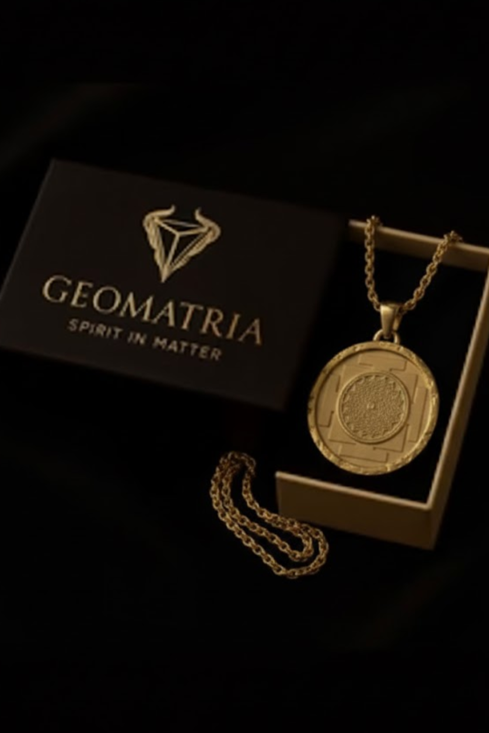 a gold necklace with a pendant, placed inside a black box with the word "Geomatria" written on it.