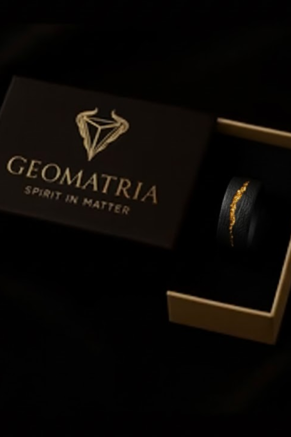 a black box with a gold logo and the text "Geomatria Spirit in Matter" on it, along with a small black ring placed inside the box.