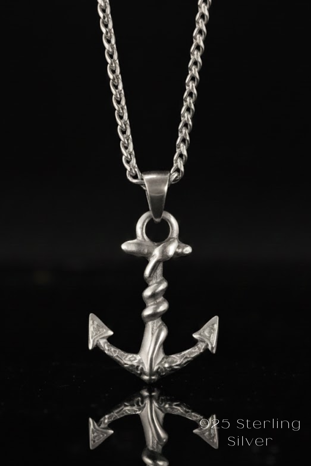 A silver-colored pendant necklace with an intricate anchor design is displayed against a black background.