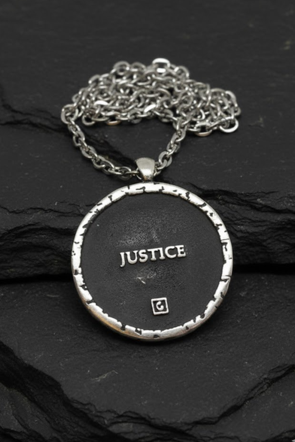 A silver-toned pendant necklace with the word "JUSTICE" engraved on a black circular background.