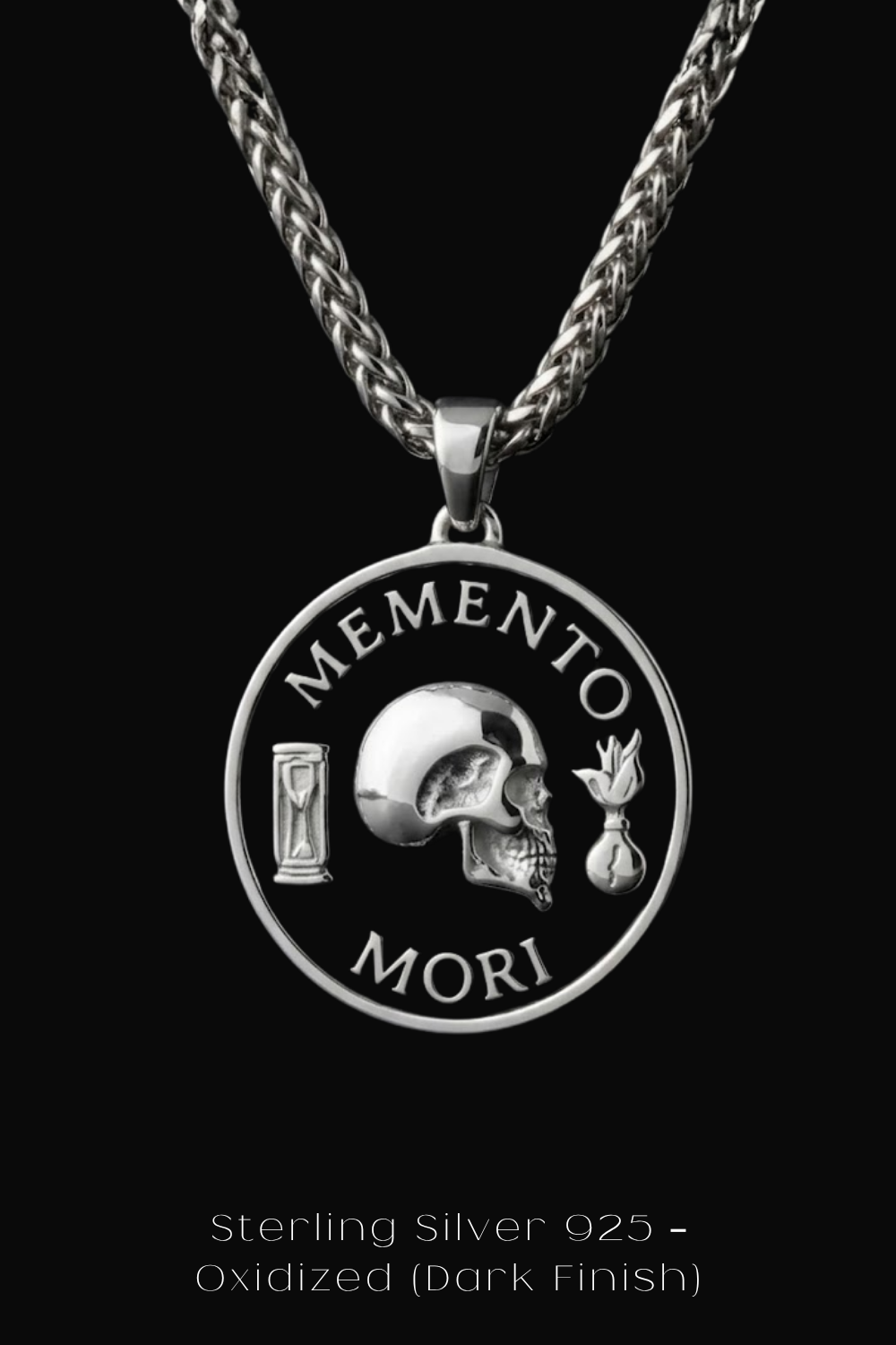A silver pendant necklace with a circular medallion featuring a skull and the Latin phrase "Memento mori" (which means " remembrance of death ").