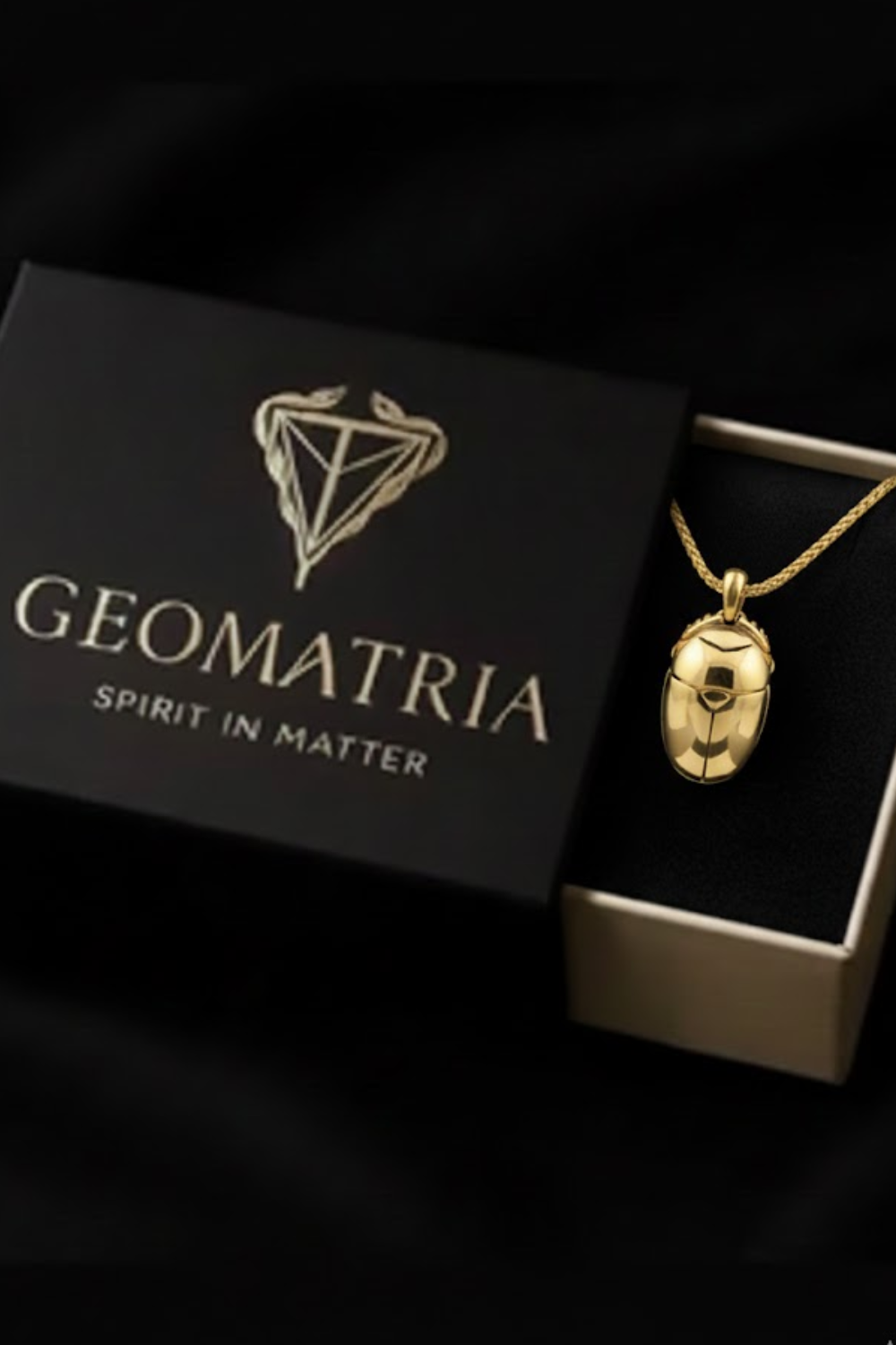 A gold necklace with a pendant is displayed in a black box with the text "Geomatria" and "SPIRIT IN MATTER" printed on it.