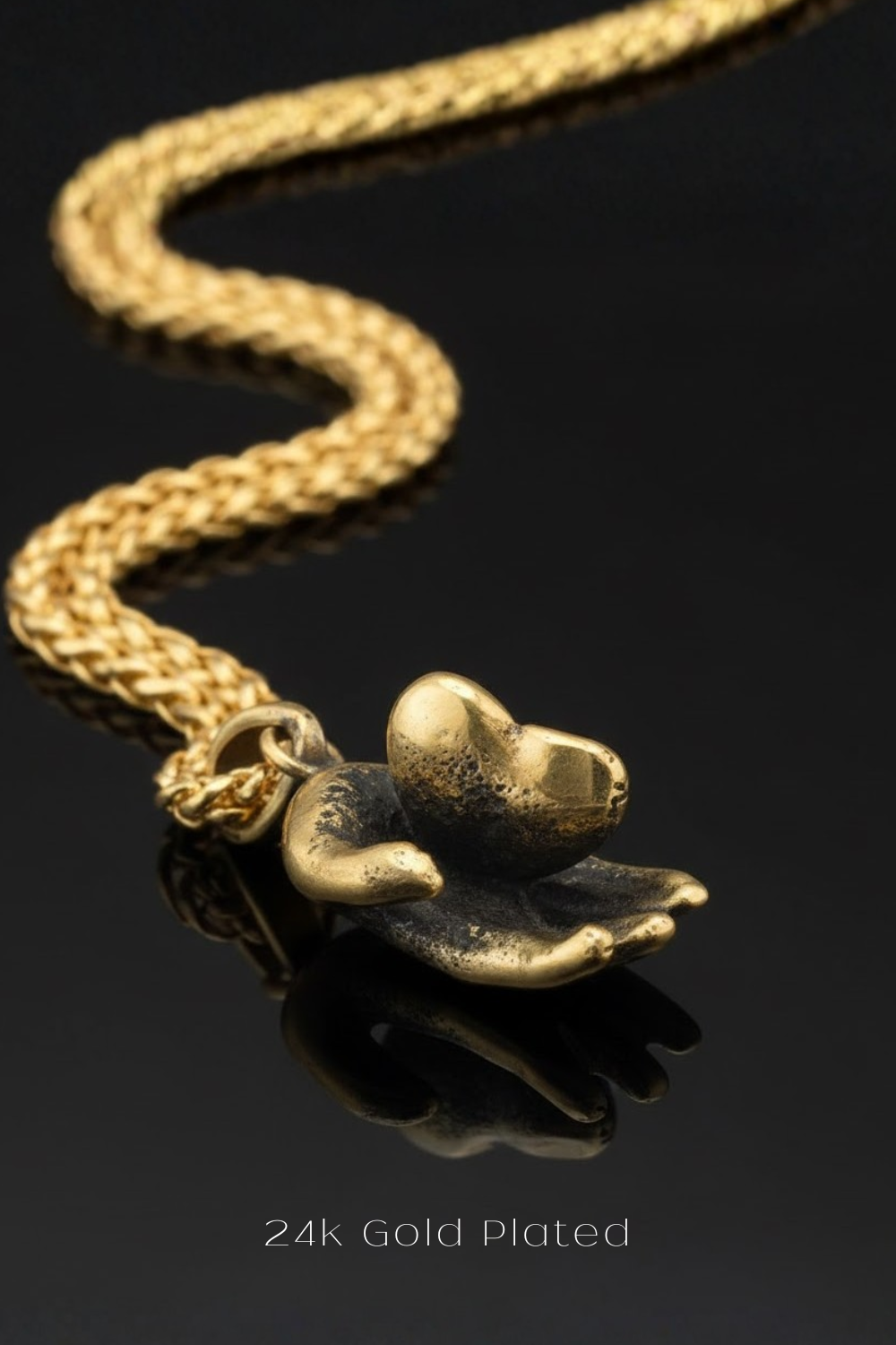A 24k gold-plated pendant in the shape of a heart, with a chain attached to it, is displayed against a black background.