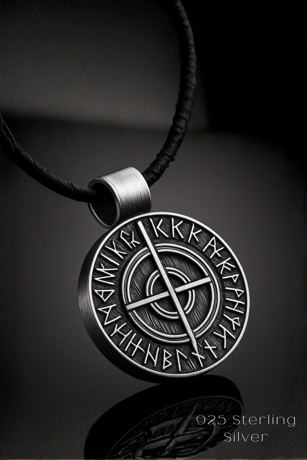 A silver pendant with a circular design featuring a cross and various symbols, suspended from a black cord.
