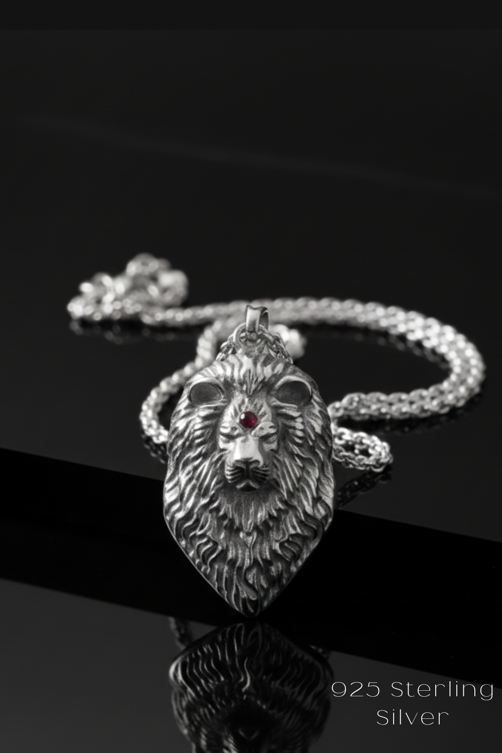 A silver pendant in the shape of a lion's head with a red gemstone, displayed on a silver chain against a black background.