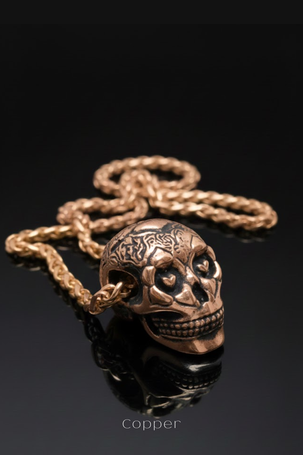 A gold-colored necklace with a pendant in the shape of a skull, resting on a reflective surface.