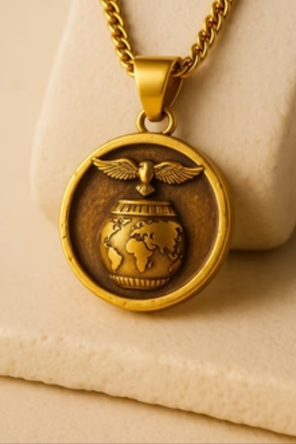 A gold-colored pendant necklace with a circular design featuring a globe and wings.