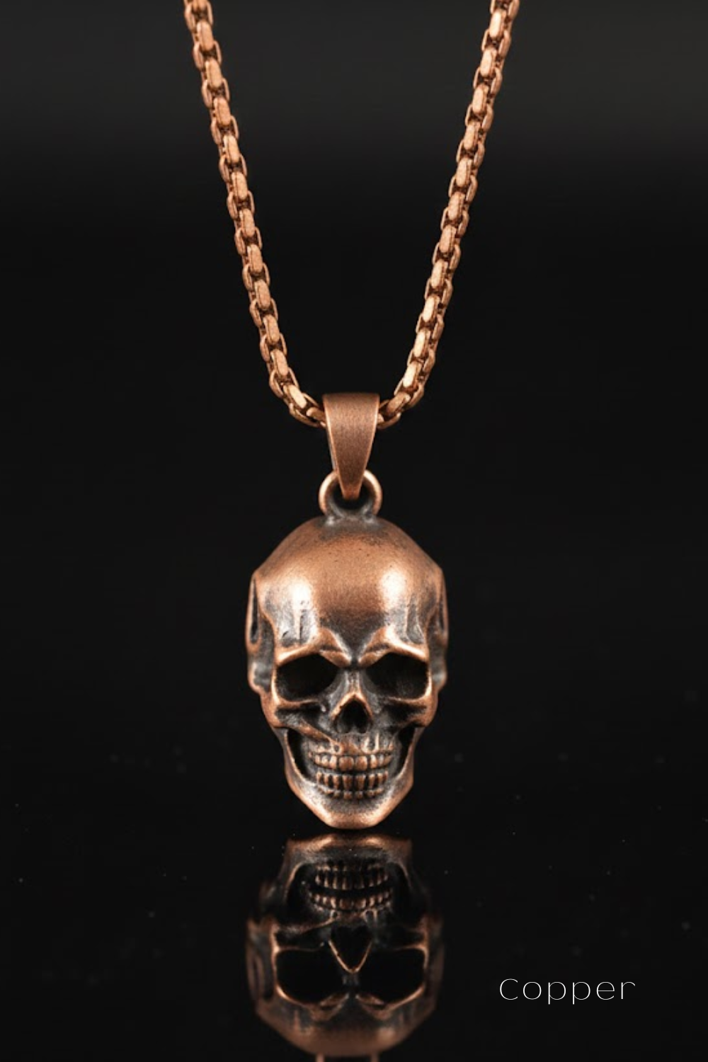 A copper-colored pendant necklace with a skull pendant is displayed against a black background.