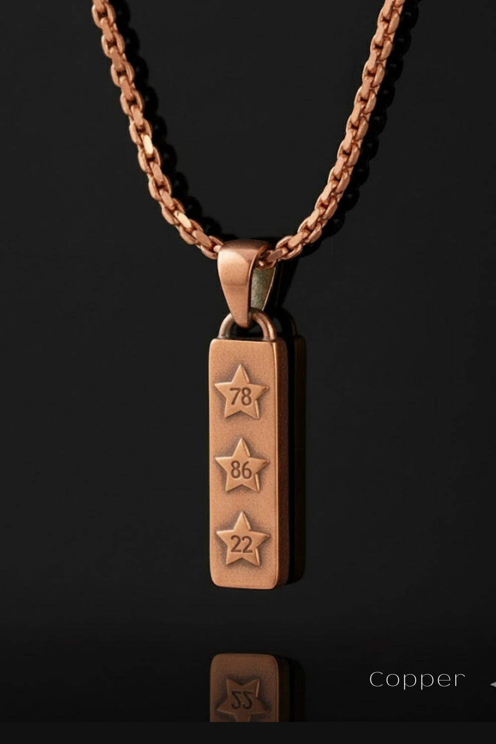 A copper-colored necklace pendant with three stars and the numbers '78', '86', and '22' engraved on it, hanging against a black background.