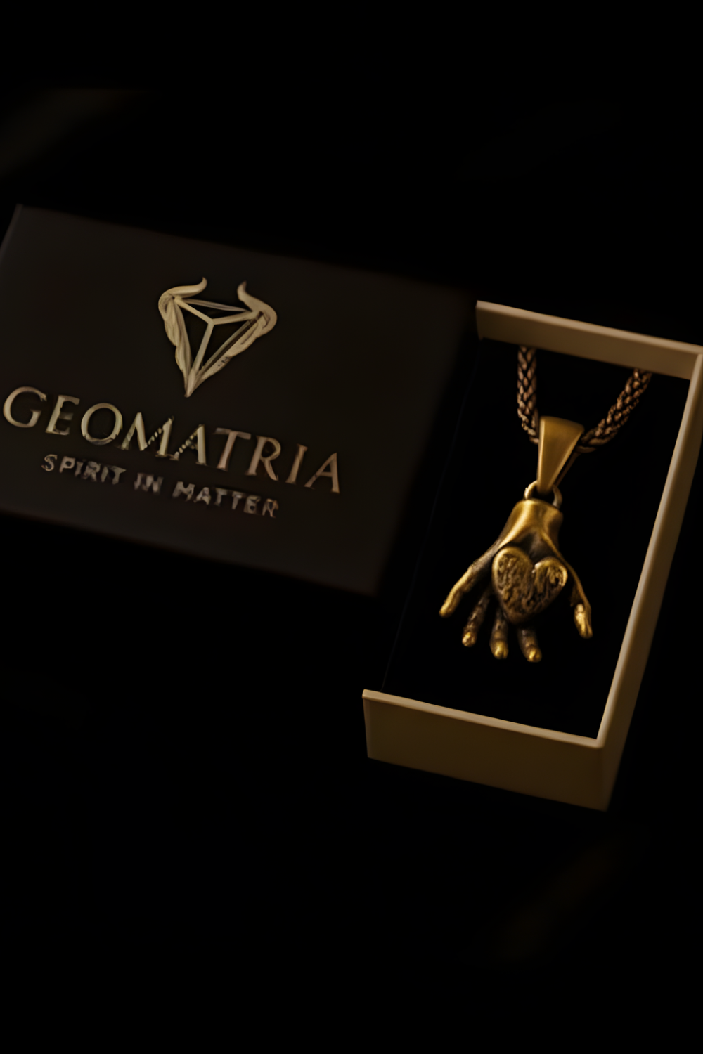 A gold-colored pendant necklace with a heart-shaped pendant is displayed in a box with the text "Geomatria Spirit in Matter" printed on it.