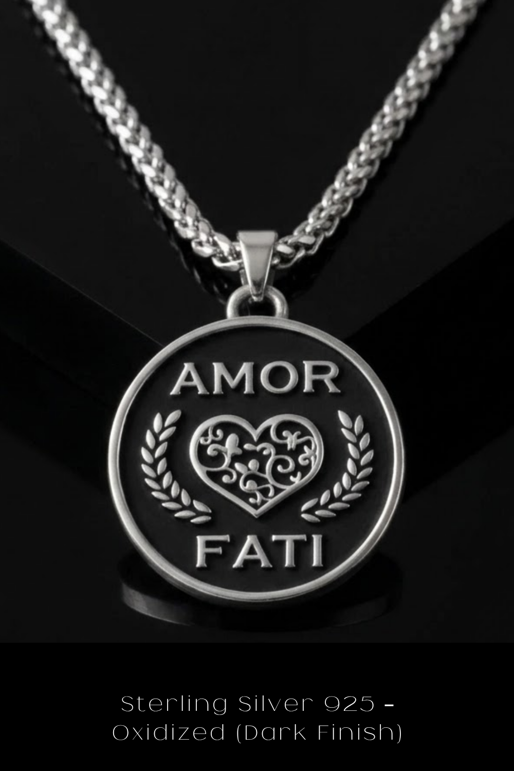 A silver pendant necklace with a circular pendant featuring the text "Amor Fati" and a heart design.