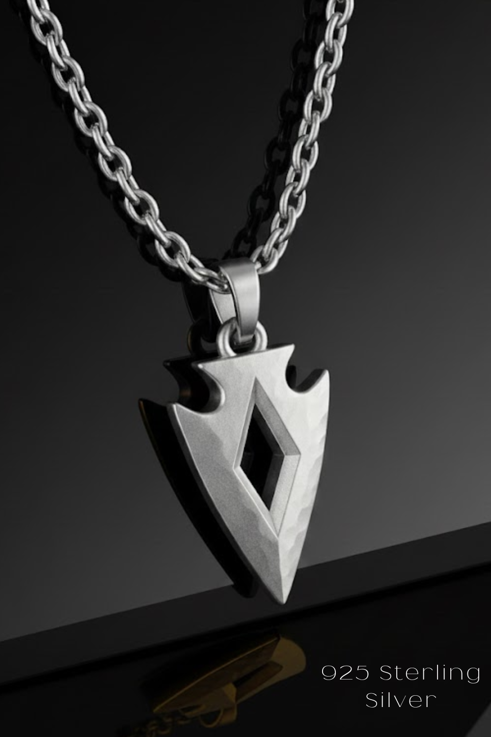 A silver-colored pendant necklace with a diamond-shaped pendant is displayed against a black background.