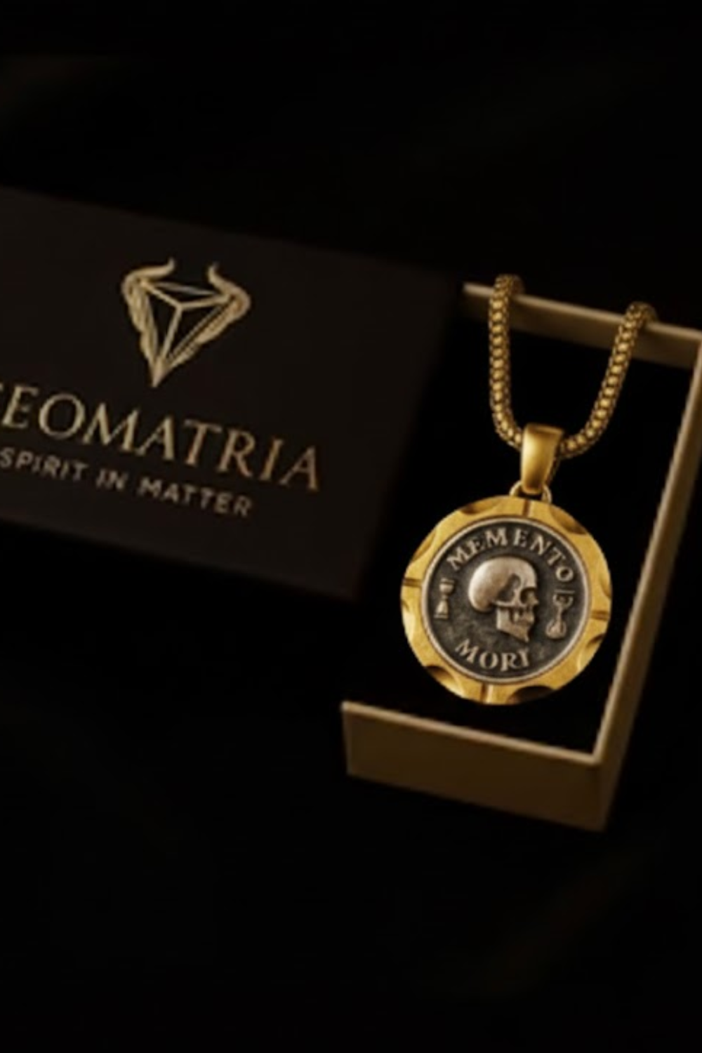 a gold-colored necklace with a pendant, displayed in a black box with the text "Geomatria Spirit in Matter" printed on it.