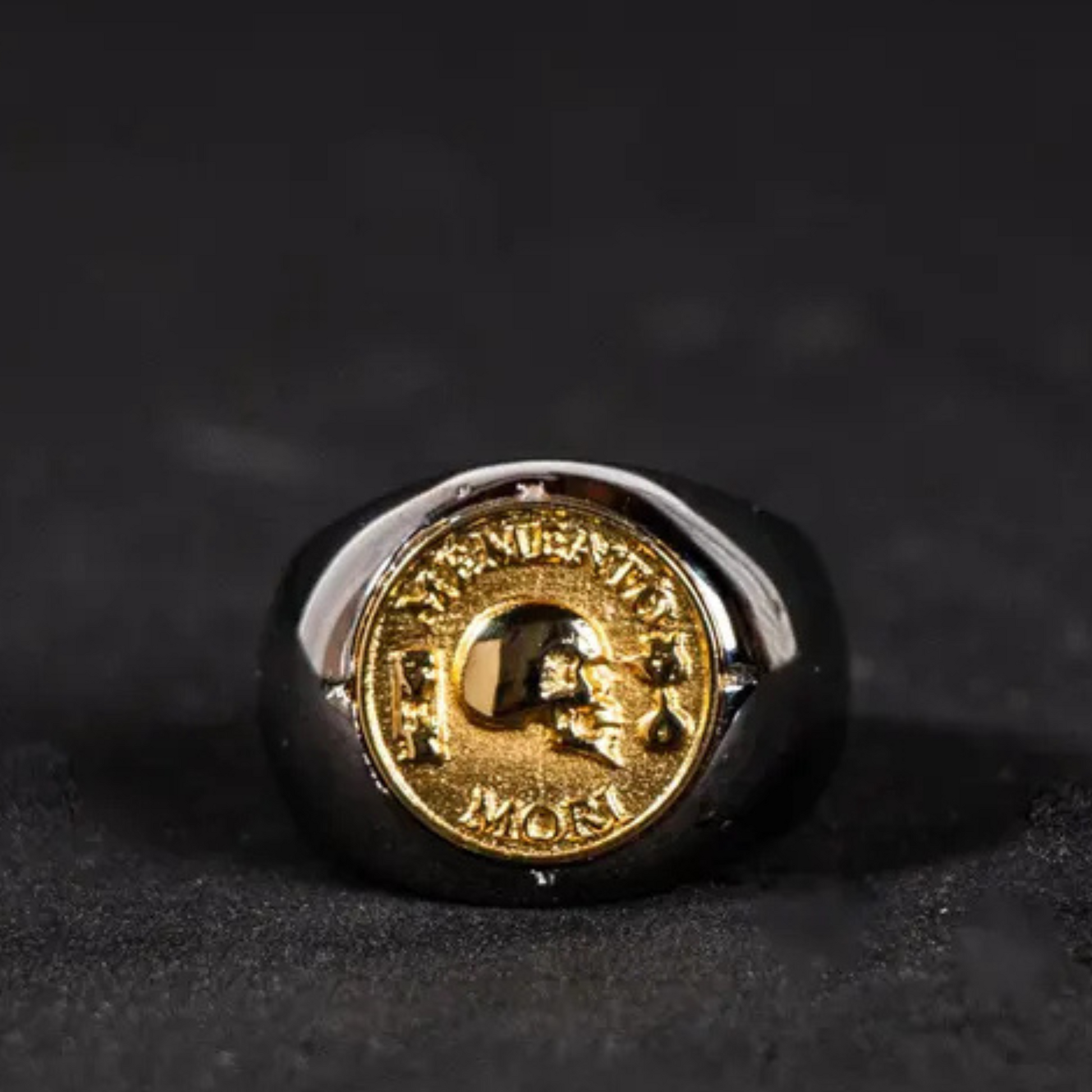 A gold-colored ring with a circular emblem featuring a skull and crossbones design.