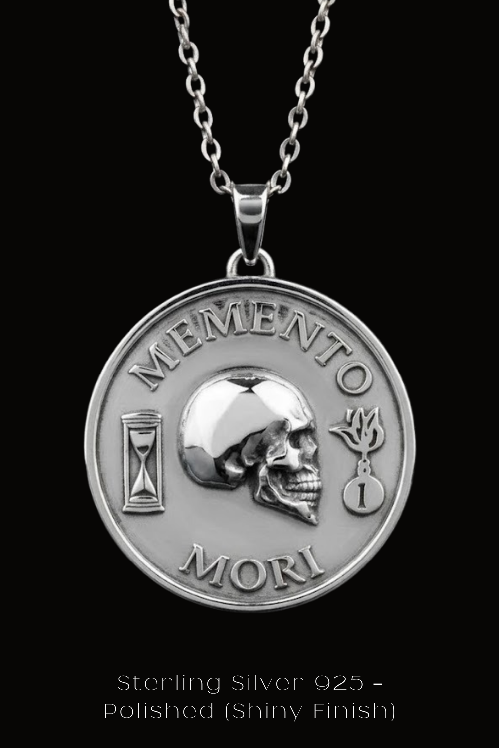 A silver medallion pendant with the text "MEMENTO MORI" and a skull design, suspended from a chain against a black background.