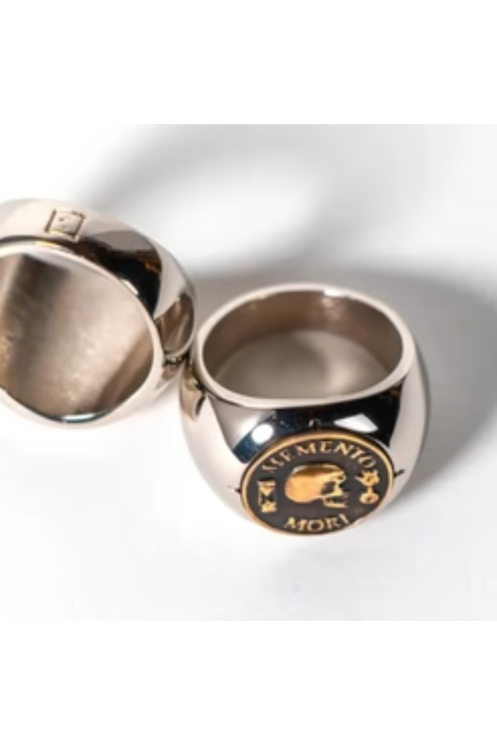 Two silver-colored rings with a gold-colored embossed design on the center, featuring the Latin phrase "SEMENIO MORI" (Saying of the Dead).