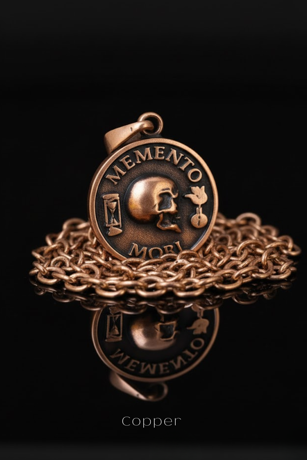 A copper-colored pendant with the Latin motto "Memento mori" inscribed on it, resting on a chain against a black background.
