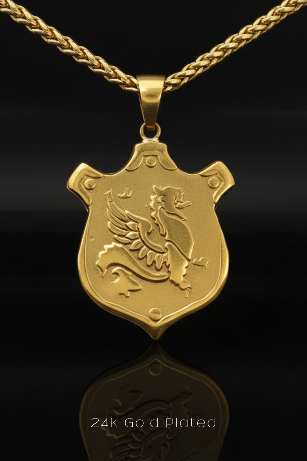 A 24k gold plated pendant featuring a shield design with a winged creature, possibly a dragon or a mythical creature, on it.