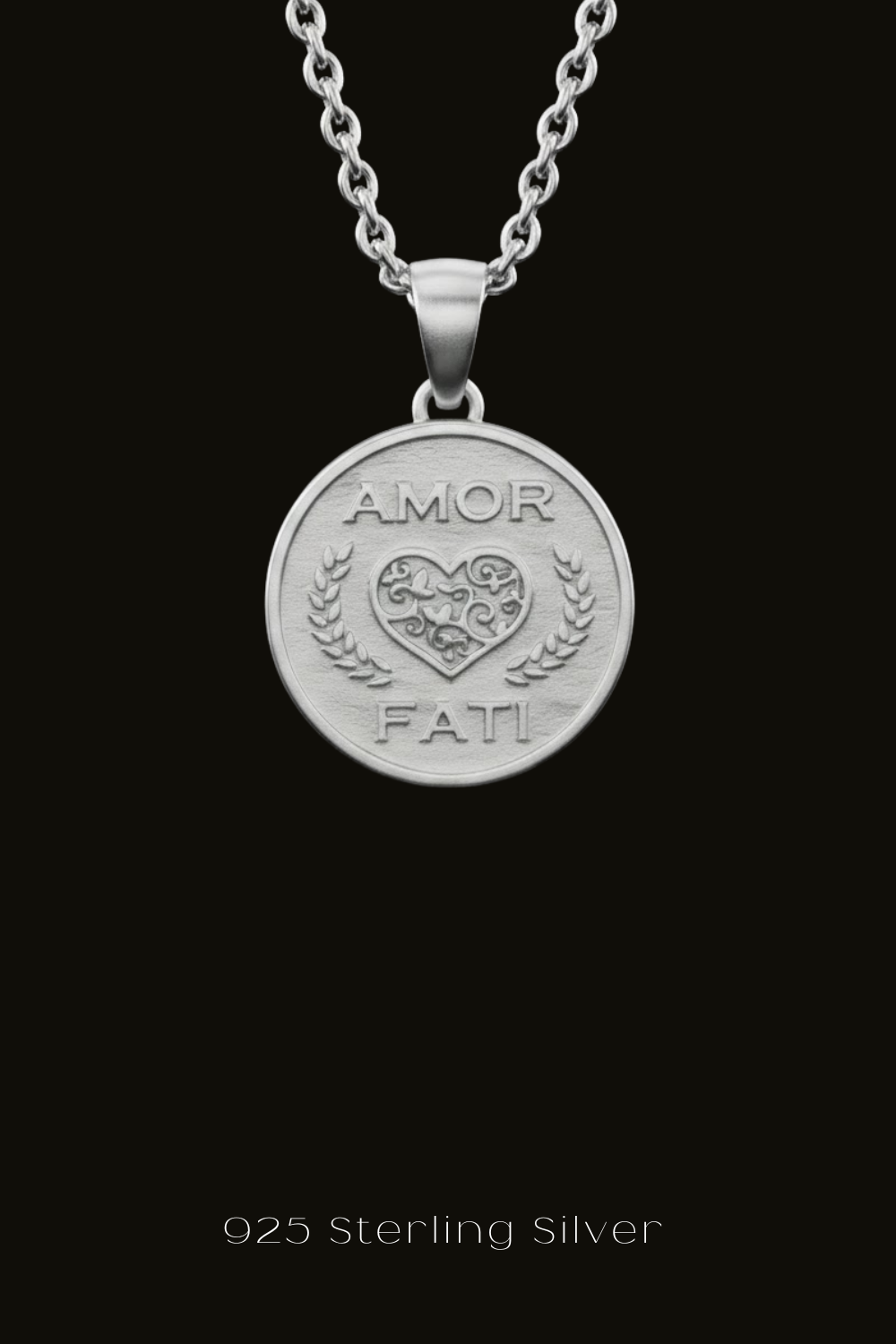 A silver pendant necklace with a heart-shaped medallion featuring the text "Amor Fati" engraved on it.