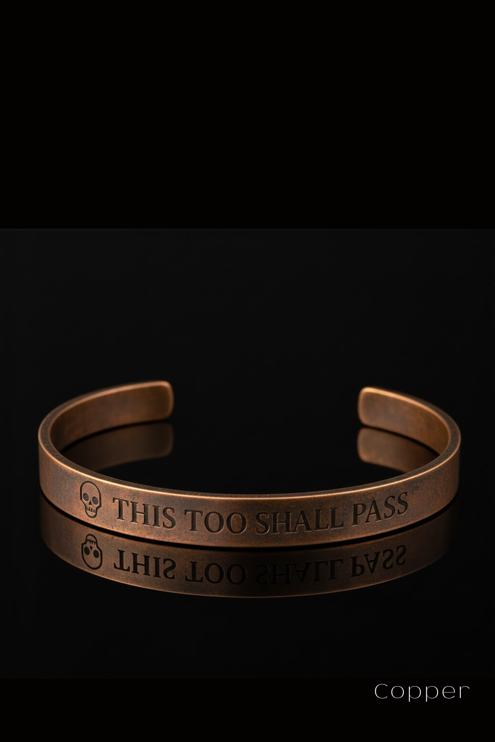 A copper bracelet with the text "THIS TOO SHARE PASS" engraved on it, against a black background.