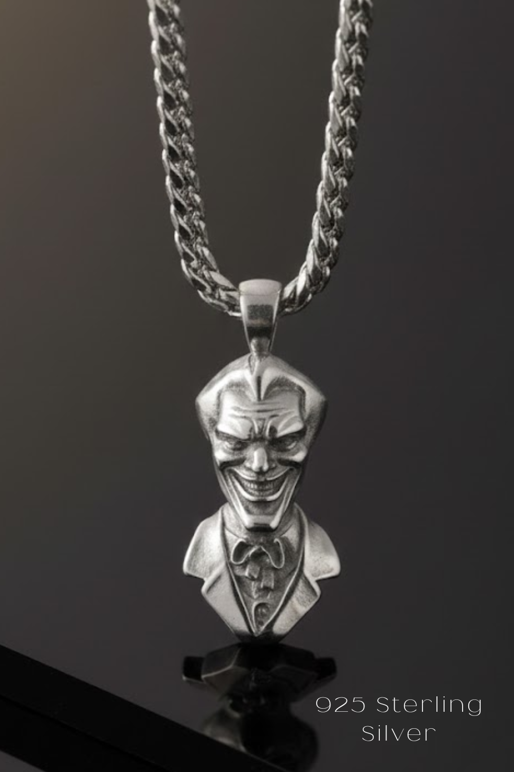 A silver-colored pendant in the shape of a smiling man's head wearing a suit and tie.