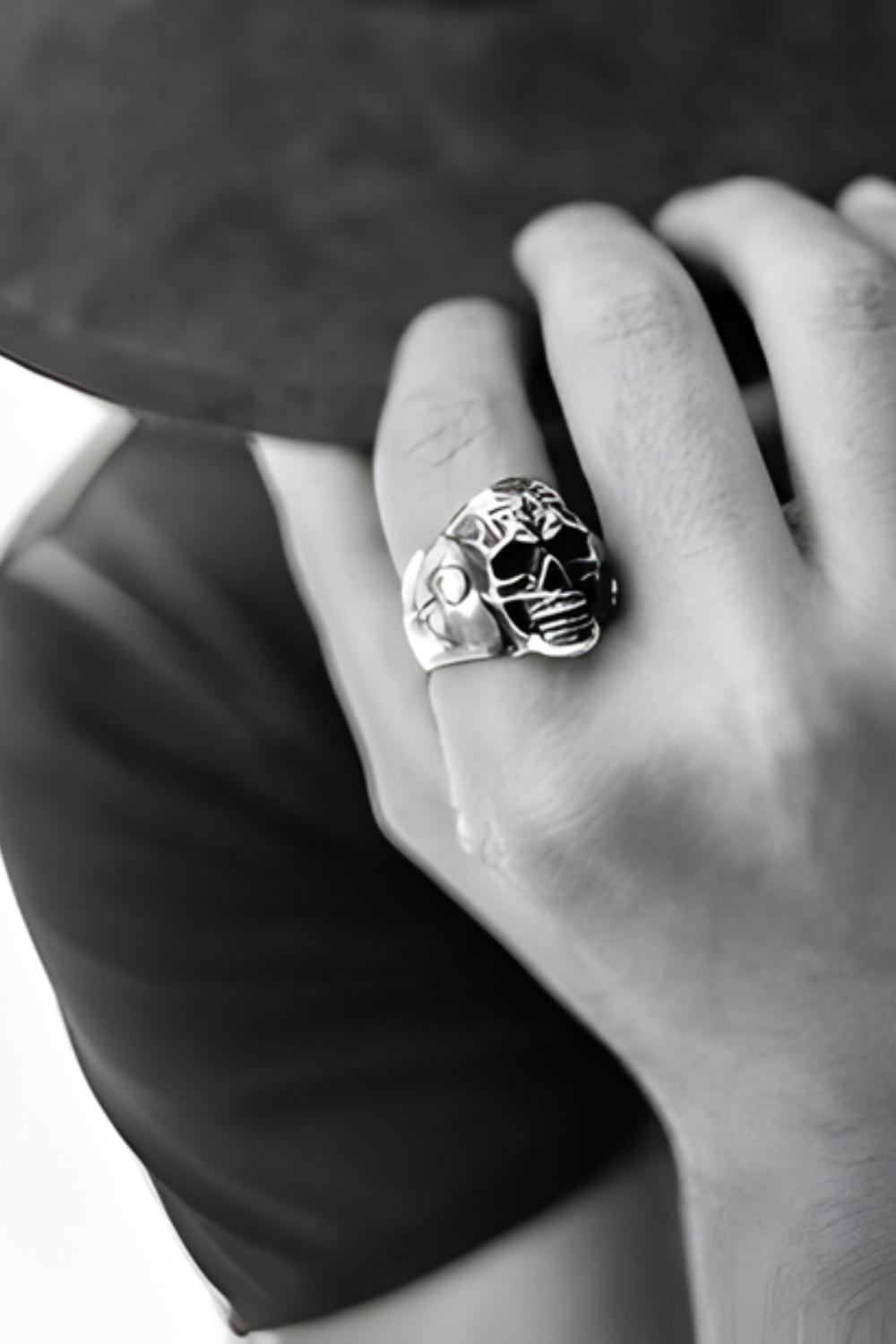 A close-up black and white image of a person's hand wearing a large, ornate ring with a skull design.