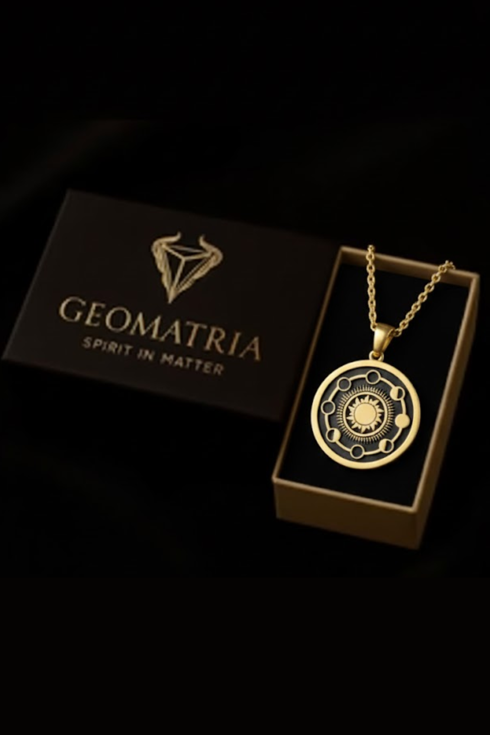 A gold-colored pendant necklace with a circular design, placed inside a black box with the text "Geomatria" printed on it.