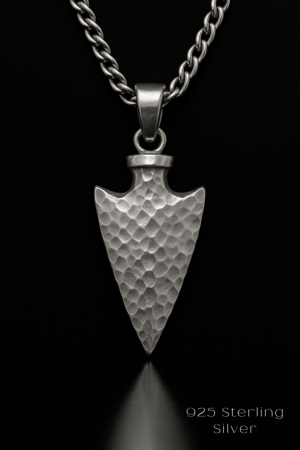 A silver pendant in the shape of an arrow, with a chain around it, is displayed against a black background.