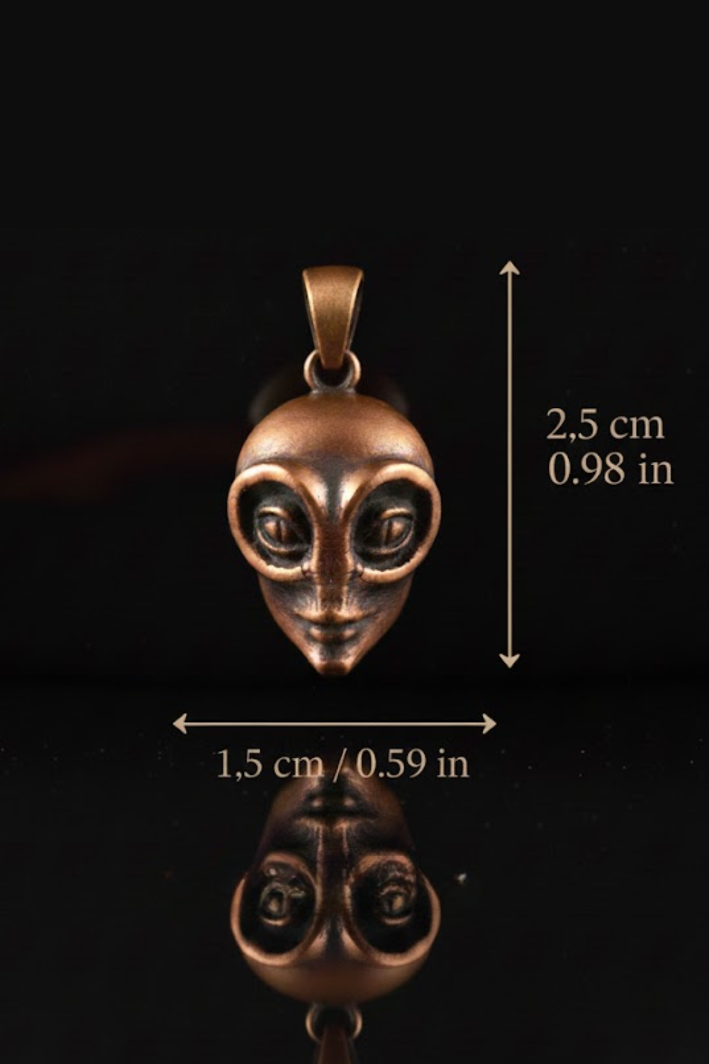 A close-up image of a bronze-colored pendant in the shape of an alien head, with measurements provided.