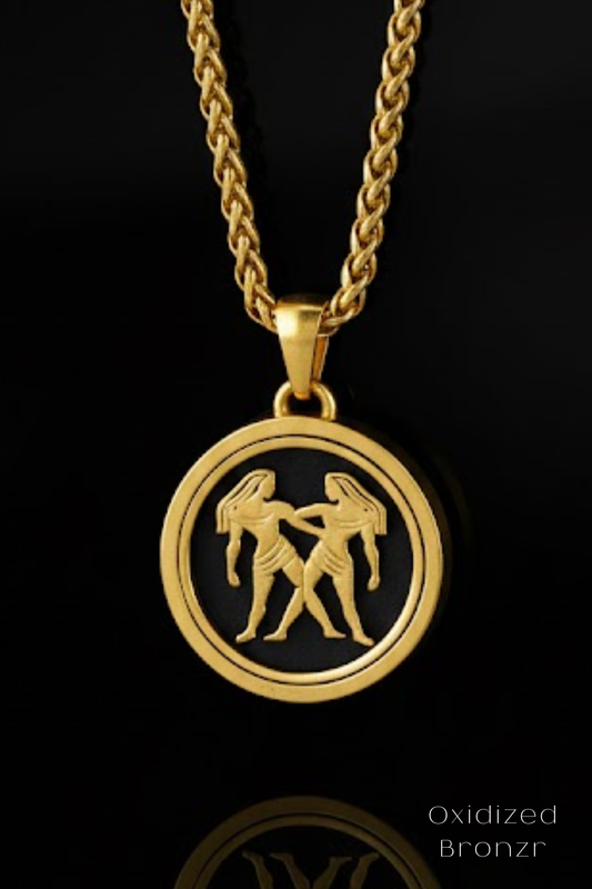 A gold-colored pendant necklace with a circular medallion featuring a design of two figures, possibly representing the astrological sign of Gemini.