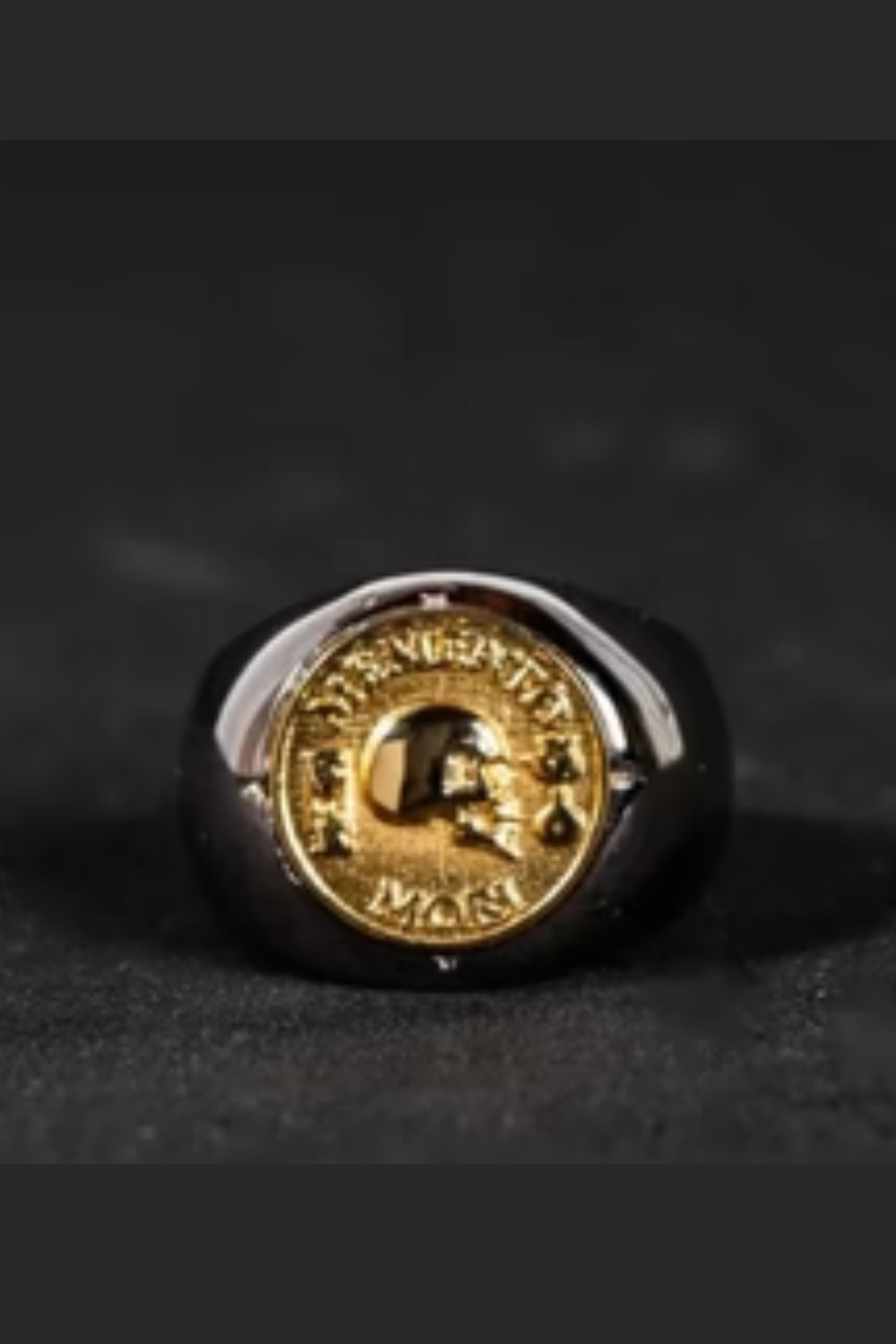 A gold-colored ring with a circular emblem featuring a skull and crossbones design.