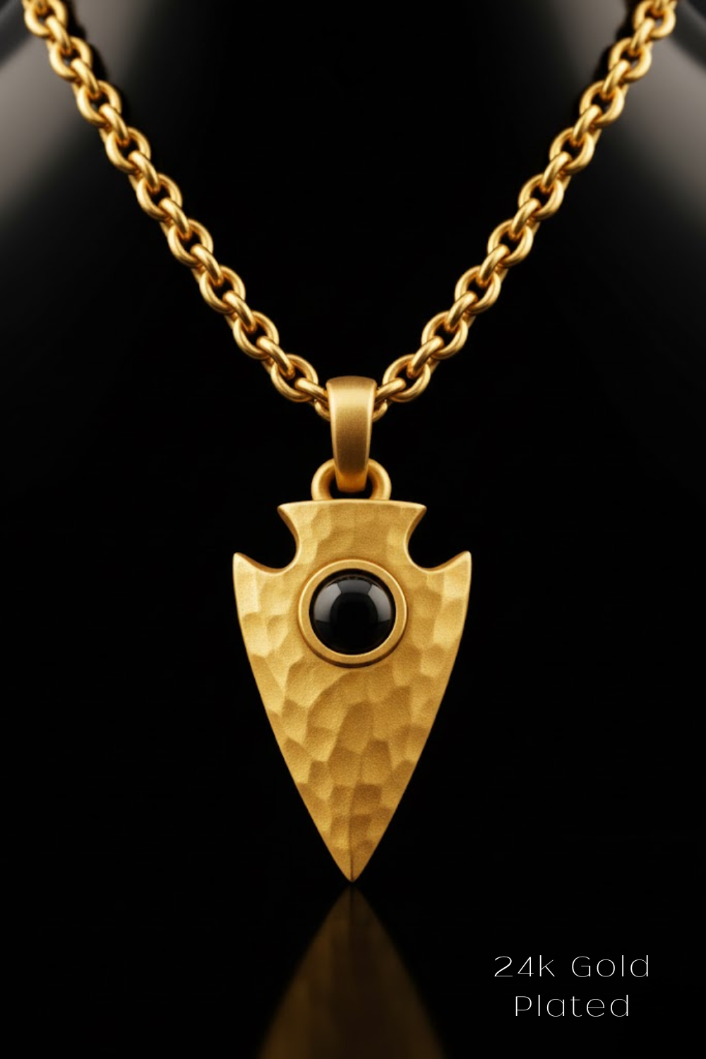 A gold-plated pendant featuring a black arrowhead with a round center stone is displayed against a black background.